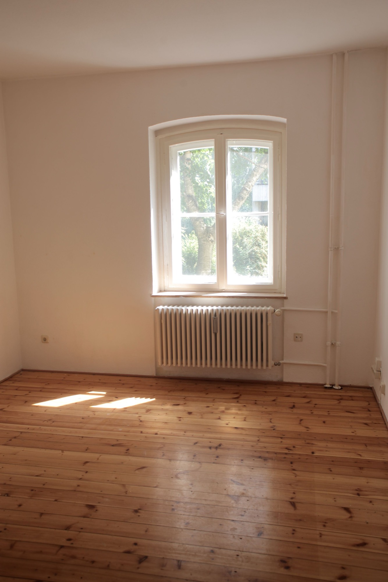 Leere Altbauwohnung mit Dielenboden und hohem Fenster